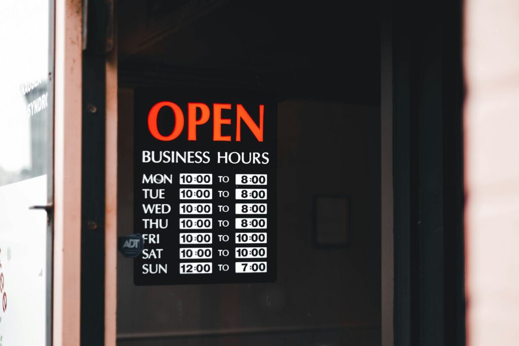 A sign that reads Open in red letters with business hours for every day of the week.